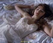 Prompt Midjourney : A young woman lies on the bed in a white wedding dress, in a designer hotel, there are calas lying next to her, there is a shampagne glass and callas, she is made up and has long eyebrows wavy hair, she is smiling, very realistic, kodak porta --v 6.0